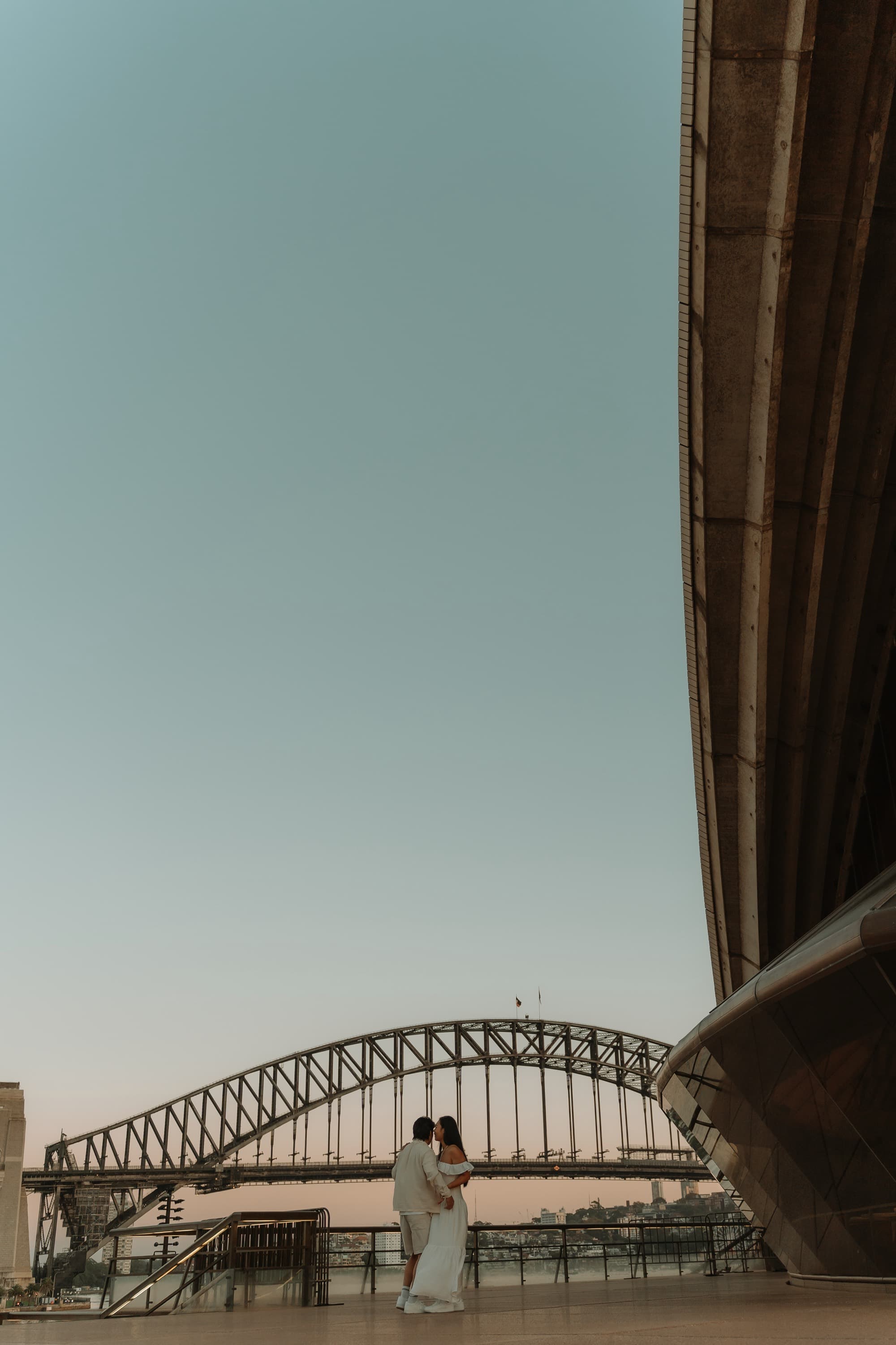 Stephanie and Terence kissing beside the Sydney Opera House, the Harbour Bridge behind them
